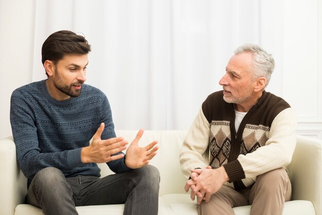 Young guy and aged man sitting on sofa