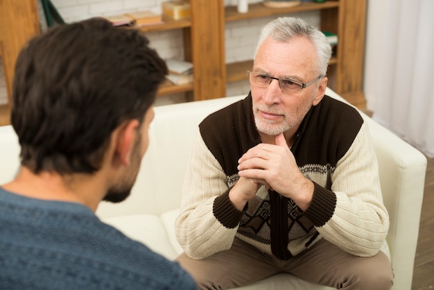 Free photo young guy and aged man on sofa in room