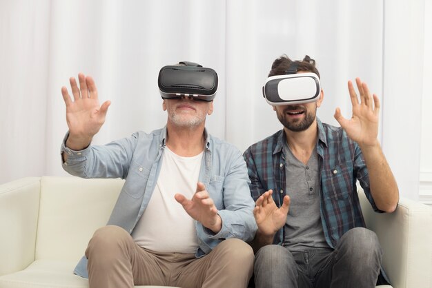 Young guy and aged man with VR glasses on sofa