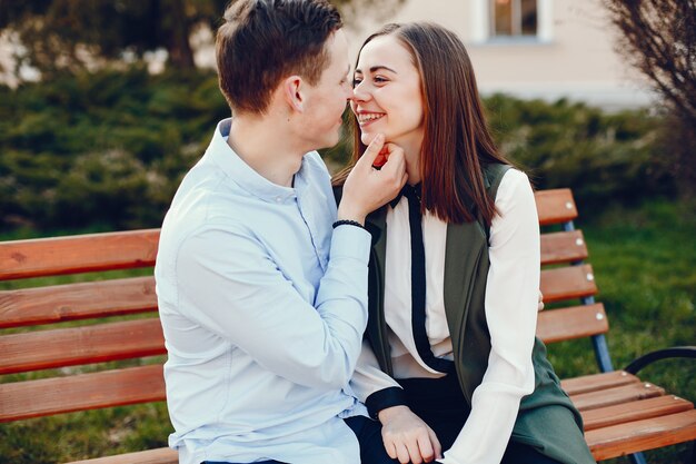 young guy in a blue shirt sitting on a bench in a sunny summer city along with her cute girl