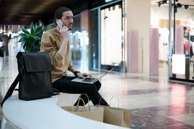 Young guy calls to a friend to tell about sales in shopping center