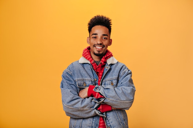 Foto gratuita il giovane ragazzo in giacca di jeans sta sorridendo sul muro arancione