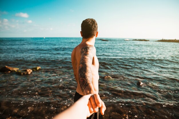 Young guy holding hands with lady near water on shore 