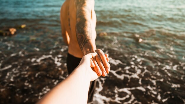 Young guy holding hands with lady near water