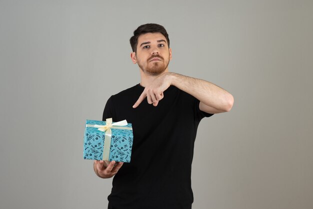 Young guy holding a present and pointing a finger at it .