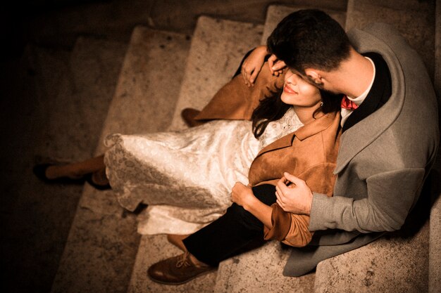 Молодой парень обнимает и целует элегантную даму, сидящую на ступеньках