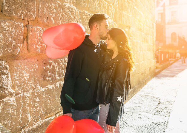 Young guy hugging and kissing lady with balloons on street