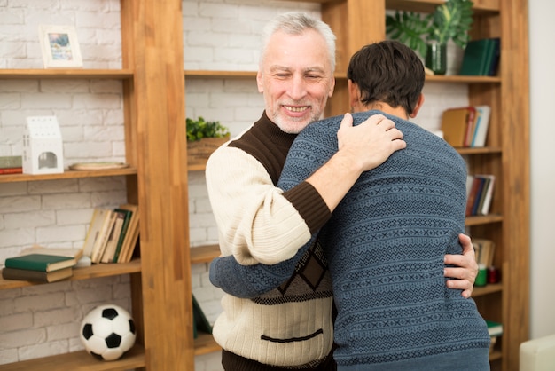 Giovane ragazzo che abbraccia con uomo sorridente invecchiato vicino a scaffali