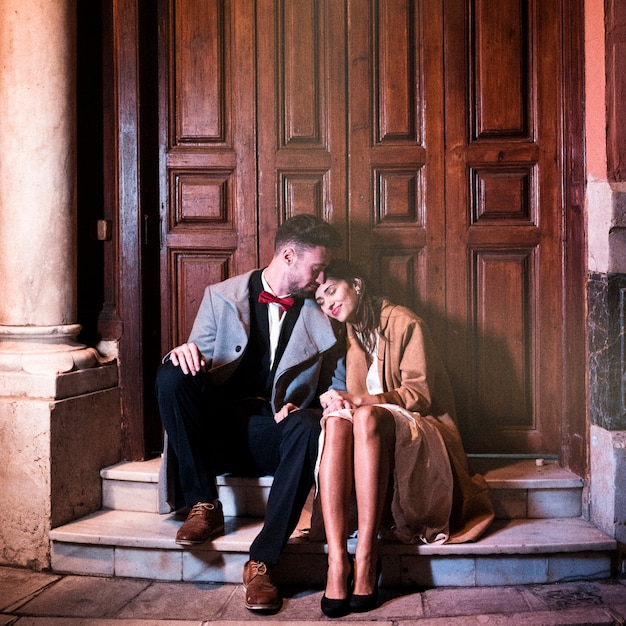 明るい女性にキスをし、通りの近くに座っている若い男