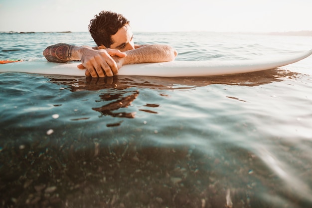 물에 서핑 보드에 누워있는 젊은 남자