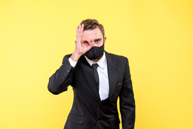 Young guy making eyeglasses gesture over yellow