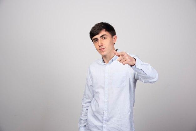 A young guy model standing and pointing at camera on gray background