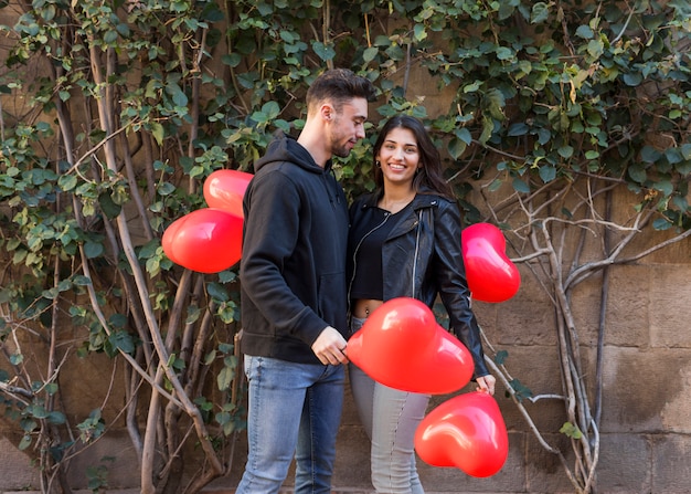 Young guy near smiling lady holding balloons in form of hearts