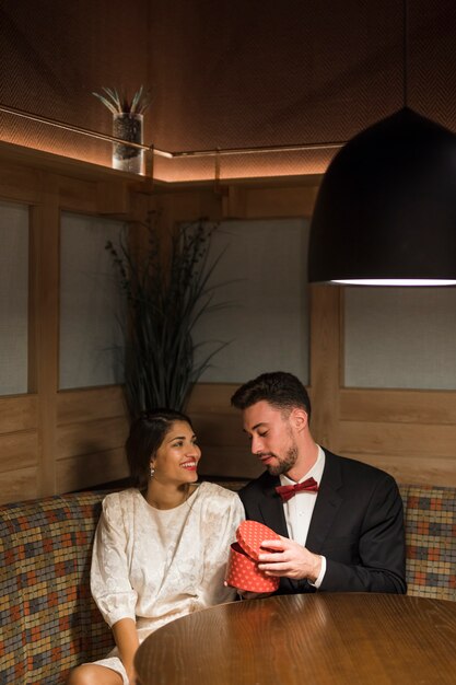 Young guy presenting gift box to attractive happy lady 