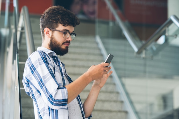 クラス間で彼のスマートフォンでソーシャルメディアのニュースを読む若い男