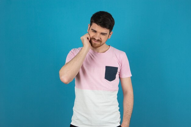 Young guy scratching his beard on a blue.