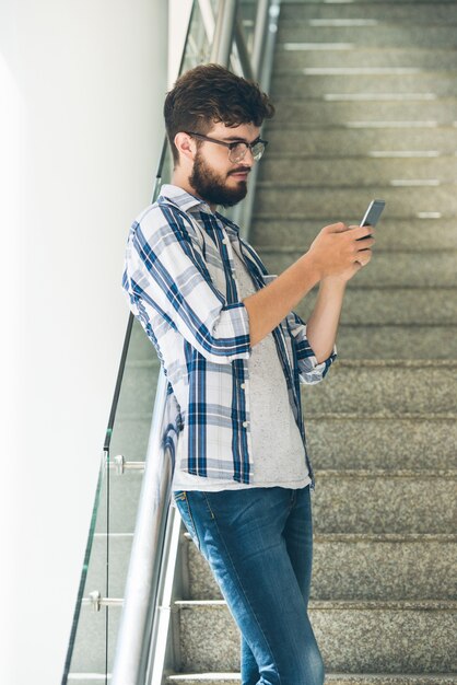 モバイルアプリを使用して大学の階段に立っている若い男