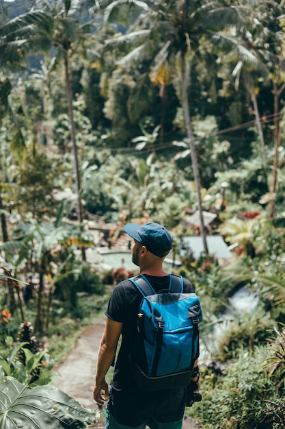 young guy with a beard and a backpack posing in the jungle in a cap