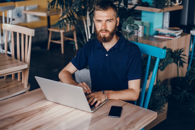 young guy with a beard works in a cafe, freelancer uses a laptop, does a project