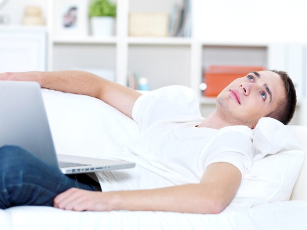Young guy with laptop look outside on the sofa