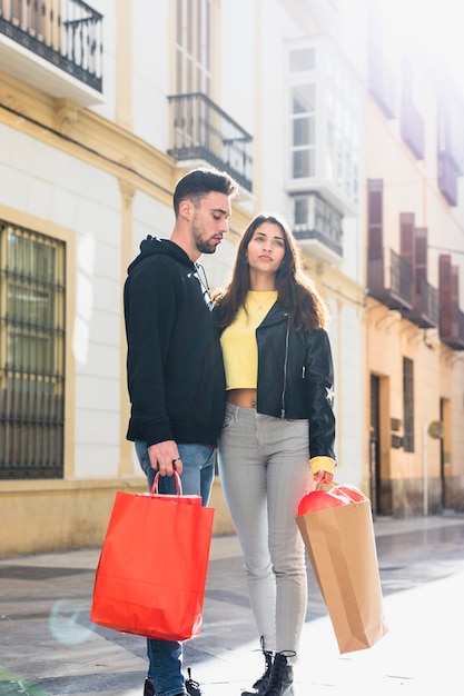 Young guy with packets embracing lady near building