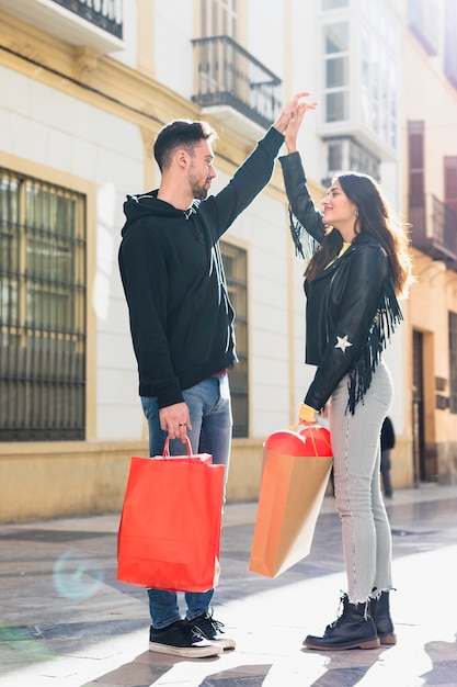 Young guy with packets holding upping hand of happy lady on street