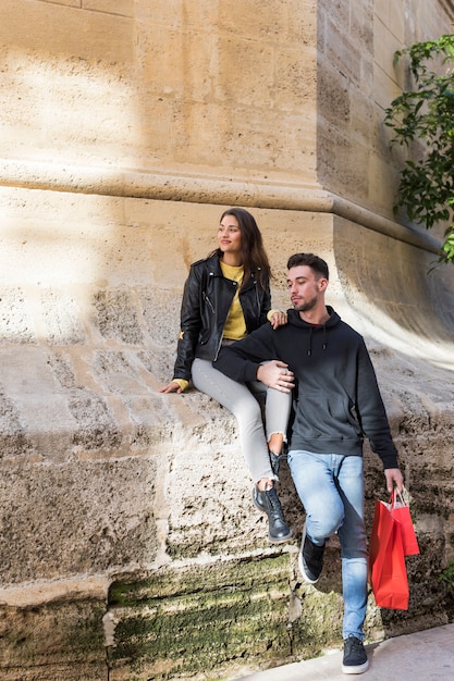 Young guy with packets hugging happy lady sitting on stone