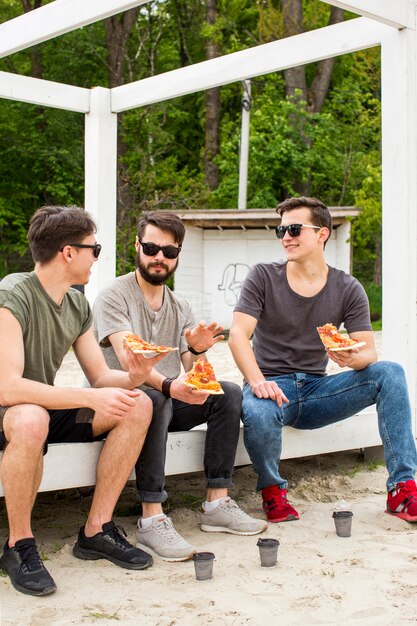 Young guys talking while holding pizza on rest