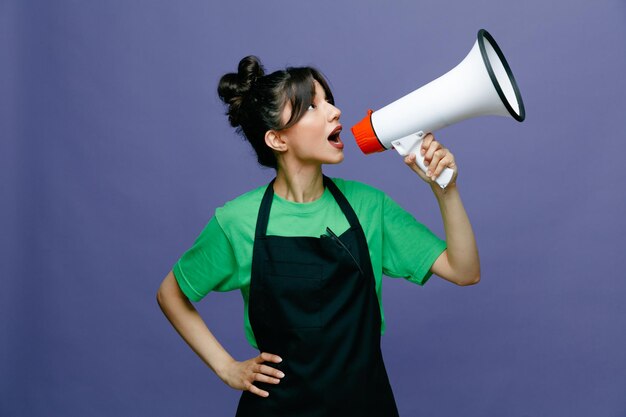 Young hairdresser woman wearing apron speaking in megaphone looking confident standing over blue background
