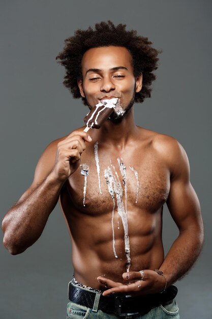 회색에 포즈를 취하는 아이스크림을 먹는 젊은 잘생긴 아프리카 남자