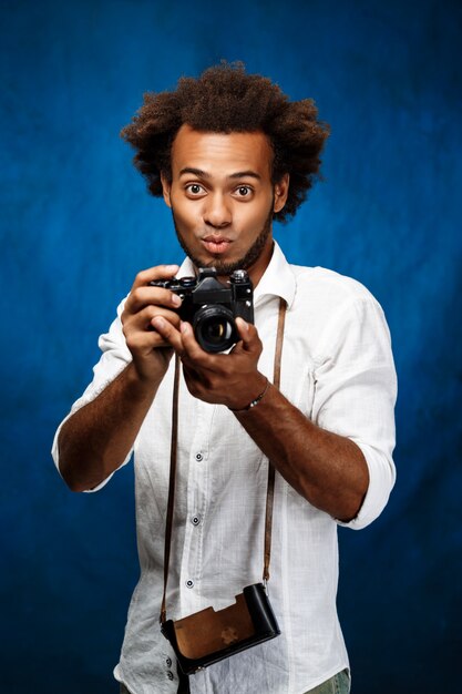 파란색 벽에 오래 된 카메라를 들고 젊은 잘 생긴 아프리카 남자.