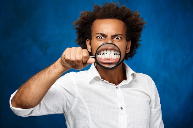 Free photo young handsome african man posing with magnifier over blue wall.