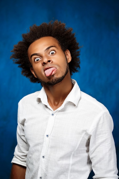 Free photo young handsome african man showing tongue, fooling over blue wall.