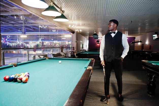 Young handsome african man wearing white shirt black vest and bow tie play pool billiard