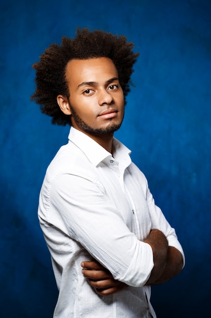 Young handsome african man with crossed arms over blue wall.