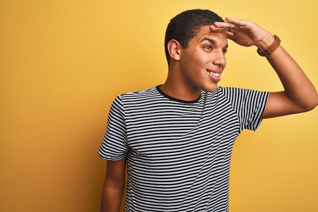 Free photo young handsome arab man wearing navy striped tshirt over isolated yellow background very happy and smiling looking far away with hand over head searching concept