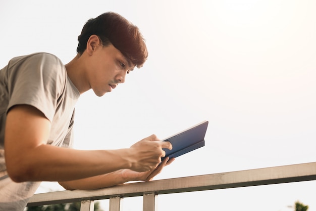 Молодая красивая азиатская книга чтения человека на балконе комнаты в свободном времени от работать дома, знания и концепции учить Premium Фотографии