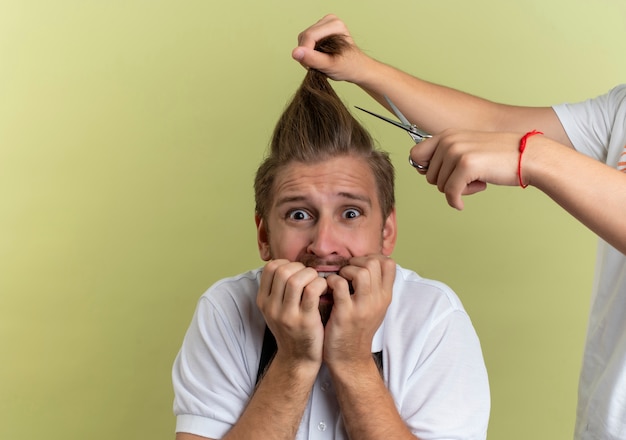 Foto gratuita giovane barbiere bello che si morde le dita spaventato di ottenere tutti i suoi capelli tagliati isolato su sfondo verde oliva con lo spazio della copia