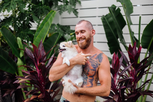 Young handsome bearded brutal tattooed happy man holds pomeranian spitz playing with lovely pet