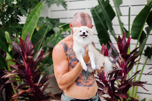 Young handsome bearded brutal tattooed happy man holds pomeranian spitz playing with lovely pet