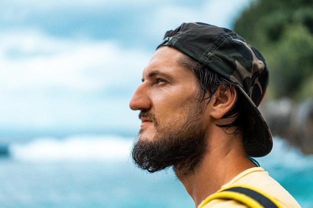 Young handsome bearded man in a cap near the ocean. Traveler with a backpack in a beautiful place.