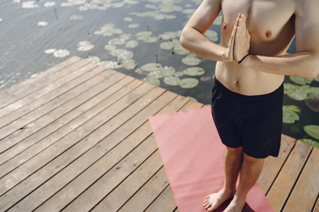 Young handsome bearded man sitting on wooden pier in summer day. Meditating and relaxing.