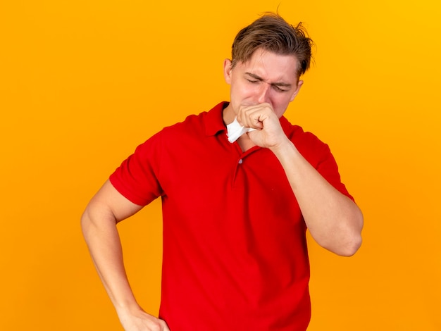 Молодой красивый блондин больной мужчина держит салфетку за рот с закрытыми глазами, изолированными на оранжевой стене
