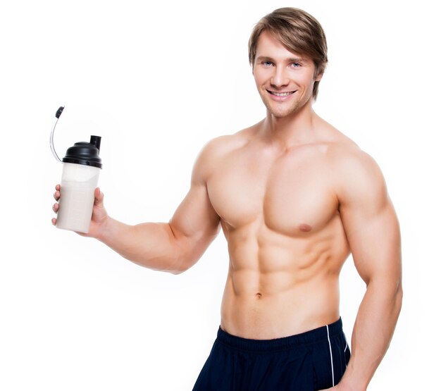 Young handsome bodybuilder with a bottle posing  on a white wall.