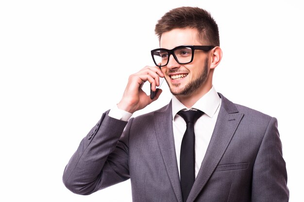 Young handsome business guy in white shirt and eyeglasses, talking on phone and smiling in reaction to colleague's joke, isolated on gray background