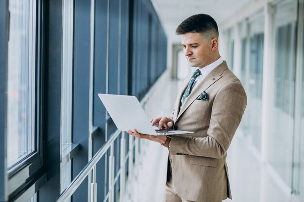 Young handsome business man standing with laptop at the office