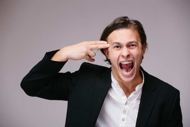 Young handsome business man wearing suit and tie over isolated wall, shooting and killing oneself pointing hand and fingers to head like gun