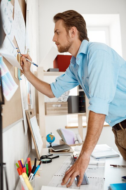 Young handsome businessman writing at the paper pinned to corkboard.