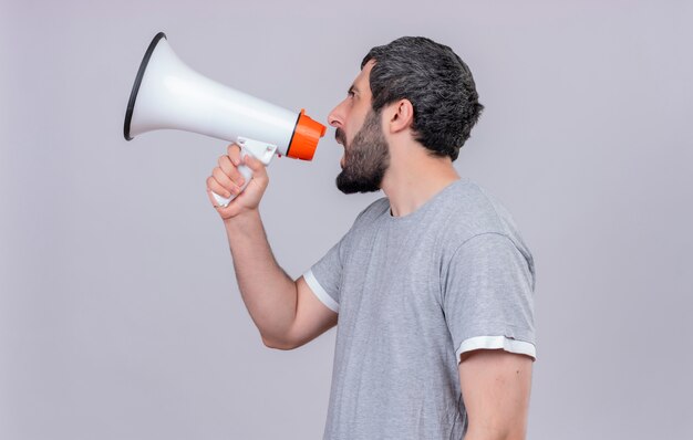 Young handsome caucasian man standing in profile view and shouting in loud speaker isolated on white background with copy space