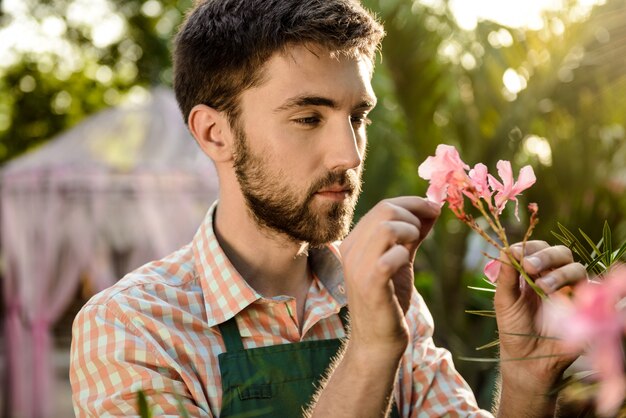 Молодой красивый веселый садовник улыбается, ухаживая за цветами